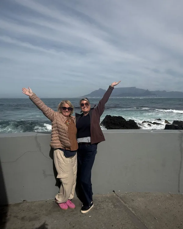 Joyce en Mirte met de armen omhoog aan zee, met de Tafelberg op de achtergrond
